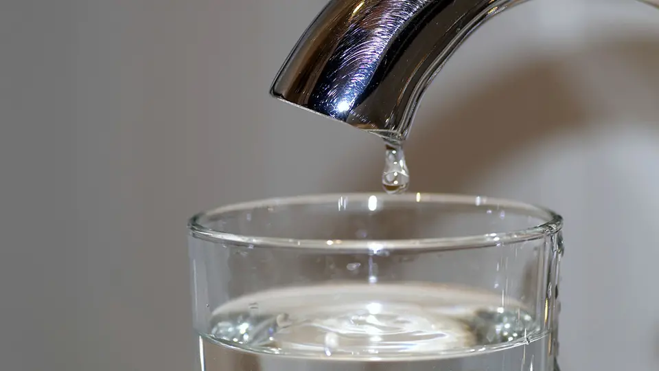 Vatten droppar från kran till ett glas