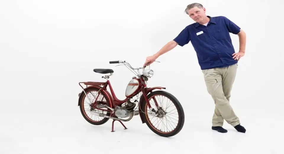 Claes Johansson står lutad mot en moped.