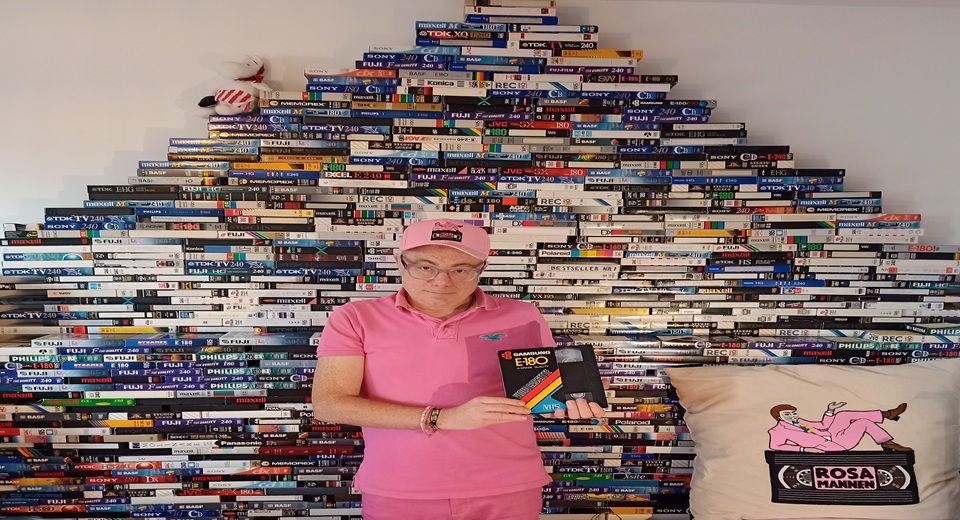 Rosa mannen står framför en vägg av VHS-kassetter