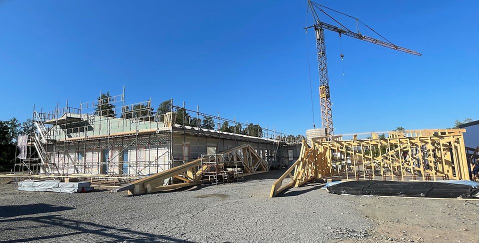 Förskolan Fagrabo i byggnation med takstolar i förgrunden och en hög byggkran, mot en blå himmel
