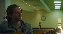 Kille som spelar gitarr sittandes i en bowlinghall. 