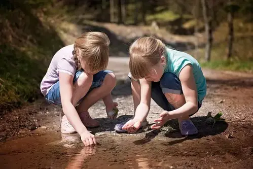 Två barn som leker vid en vattenpöl